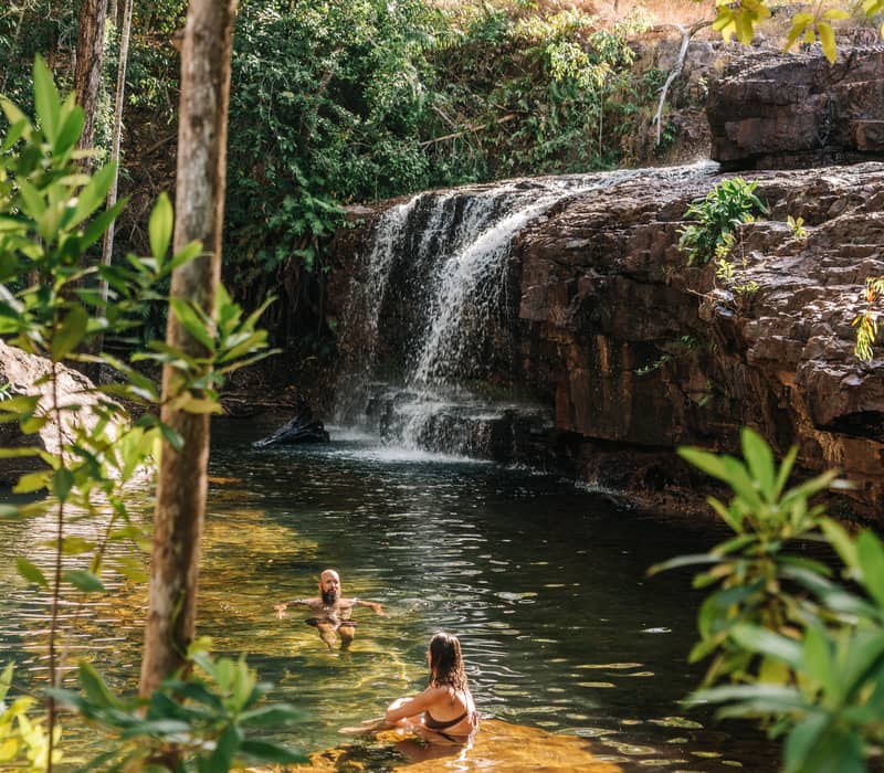 A couple enjoys a peaceful swim in the clear, sun-dappled waters of the Lower Cascades, framed by the lush monsoon forest of Litchfield National Park.