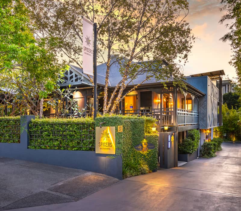 A modern luxury hotel bedroom with floral curtains, blue velvet pillows, and a designer bedside lamp.