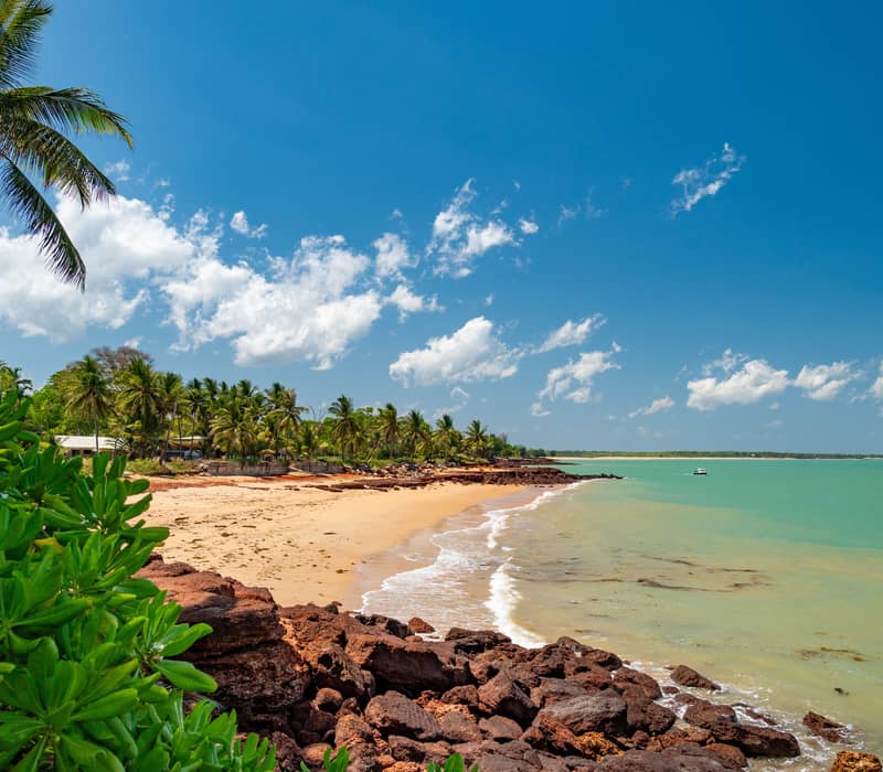 Aerial view of a tropical beach at Dundee Beach with red rocky outcrops, golden sand, and calm turquoise water.