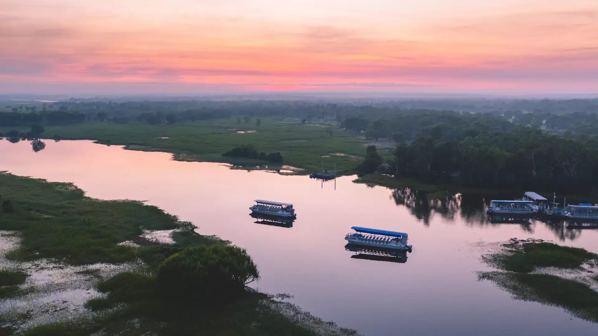 A stunning aerial view captured by Salty Wings, showing tour boats on the mirrored surface of Yellow Water Billabong as the sun rises over the Kakadu wetlands.