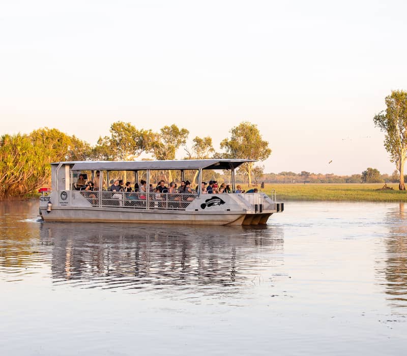 A group of visitors aboard a flat-bottomed tour boat experiencing a guided cruise through the lily-covered wetlands of Yellow Water Billabong in Kakadu National Park.