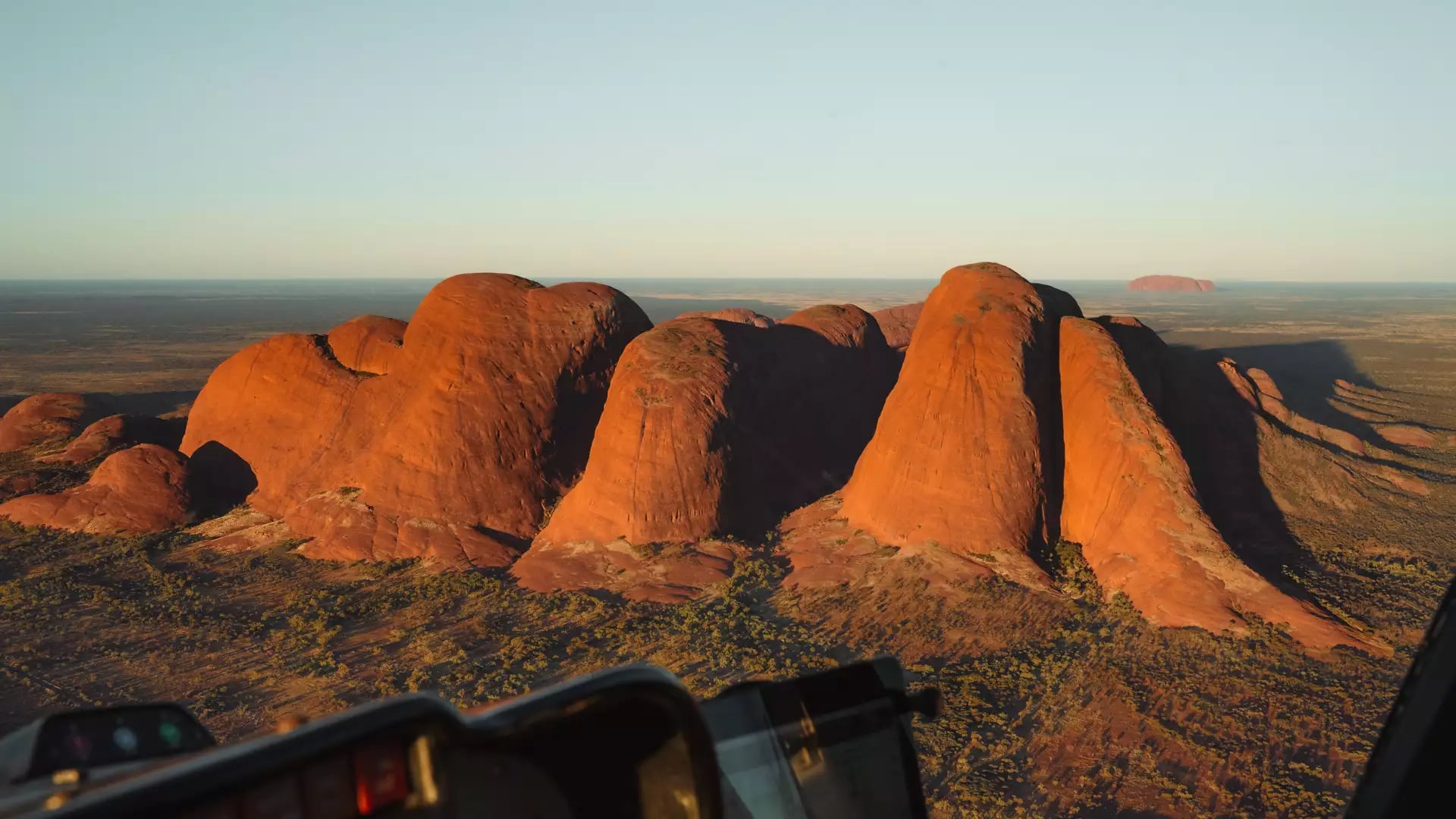 A stunning aerial perspective of the ancient conglomerate rock domes of Kata Tjuta, captured at golden hour from a helicopter cockpit.