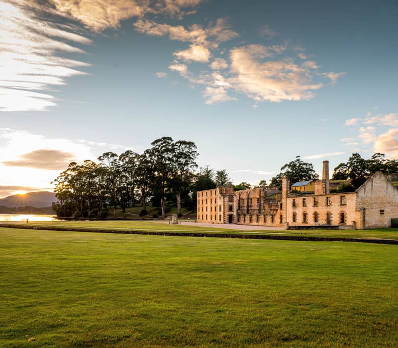 A wide, scenic view of the Port Arthur Historic Site ruins at sunset.