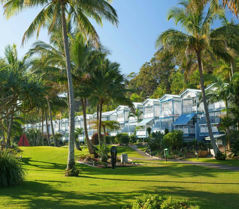White villas with blue awnings among palm trees and green lawns at Tangalooma Island Resort.